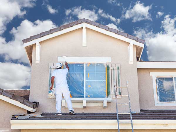 Worker painting the top window trim on the exterior of a home